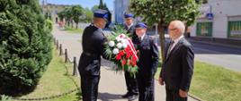 Strażacy oraz jedna osoba cywilna składają kwiaty przy pomniku.