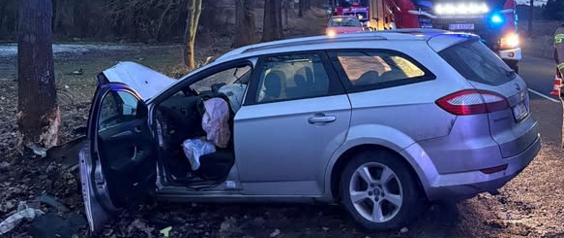 samochód osobowy rozbity na poboczu, w tle wóz strażacki