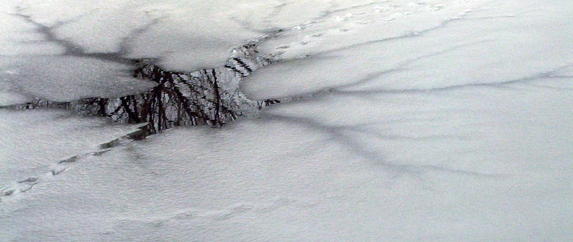 Zdjęcie przedstawia staw na którym widoczna jest bardzo cienka warstwa lodu. Jest to przestroga dla wchodzących na lód w takich miejscach.