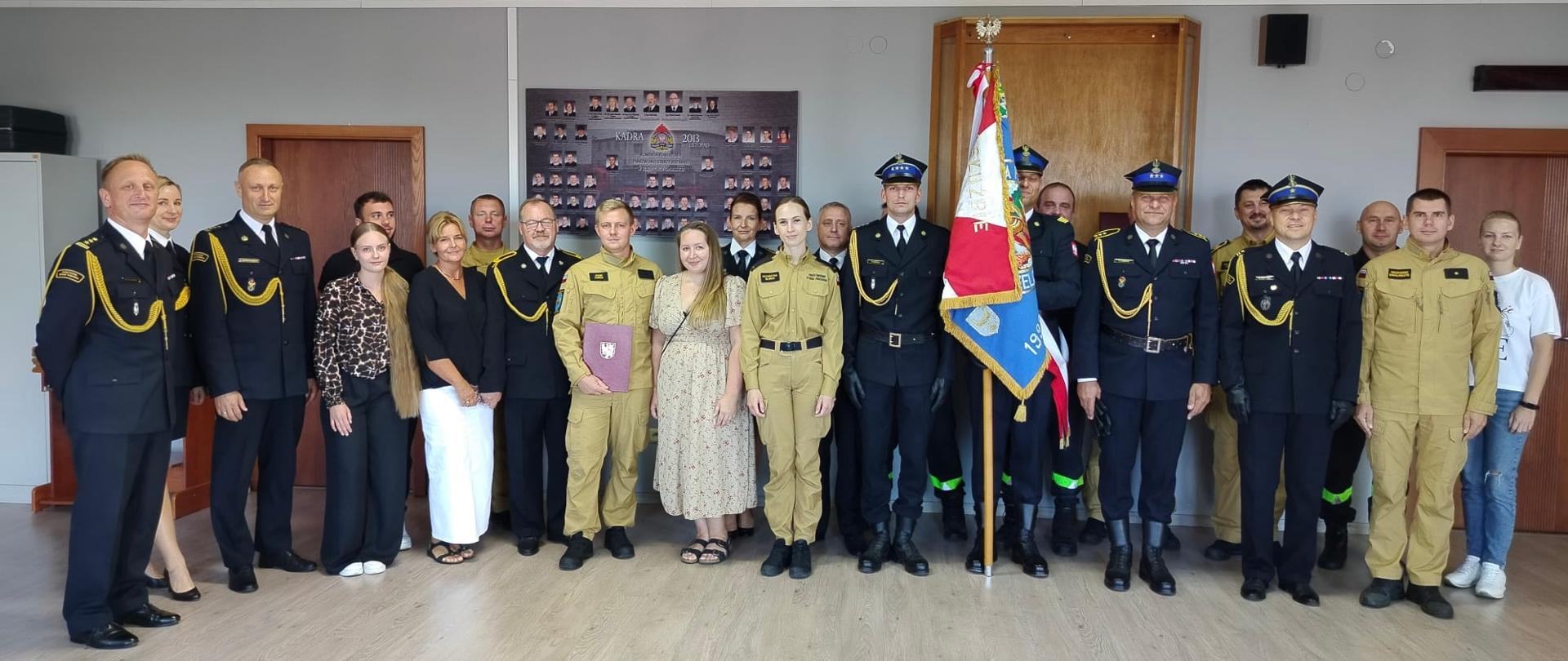 Na zdjęciu znajdują się osoby ubrane w mundury, ubrania służbowe i cywilne. Znajduje się poczet sztandarowy. Wszyscy są ustawieni do zdjęcia