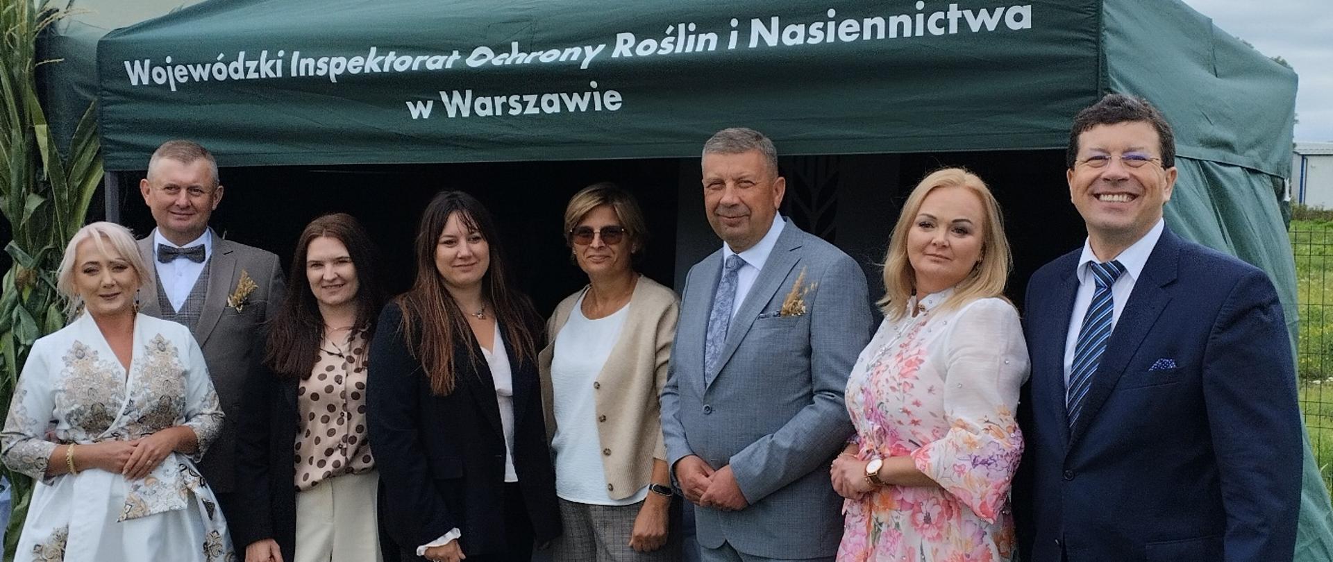 Grupa pracowników i gości stojąca przed zielonym namiotem Wojewódzkiego Inspektoratu Ochrony Roślin i Nasiennictwa w Warszawie.