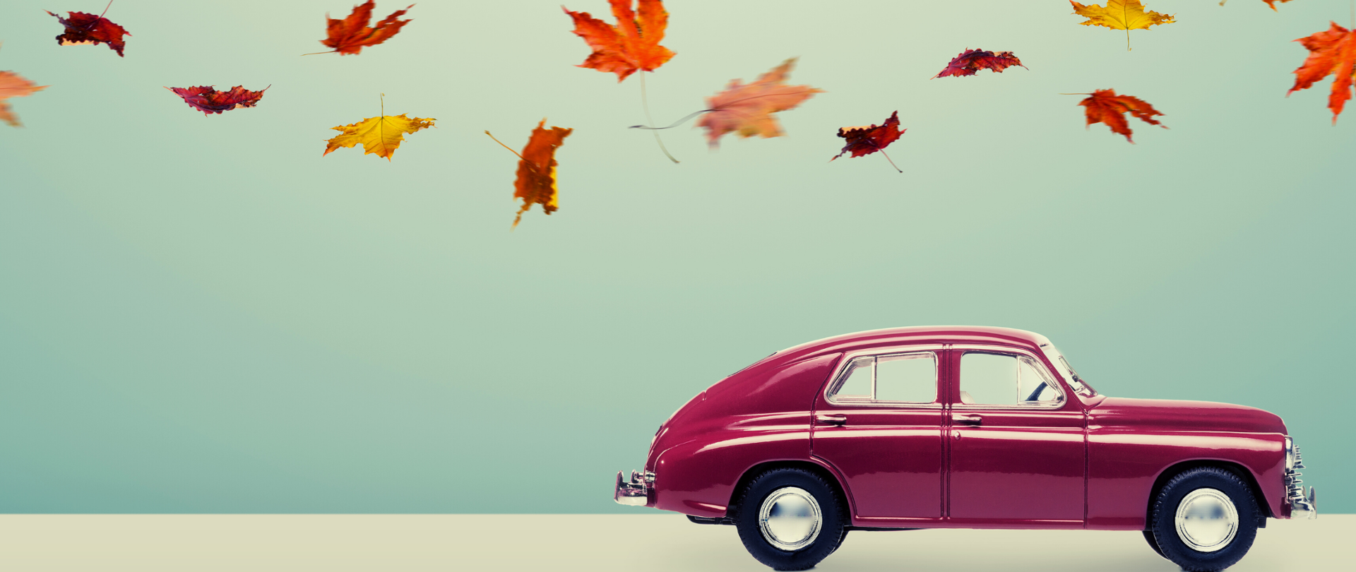 Ciemnobordowe retro auto na niebieskim tle, nad nim jesienne liście.