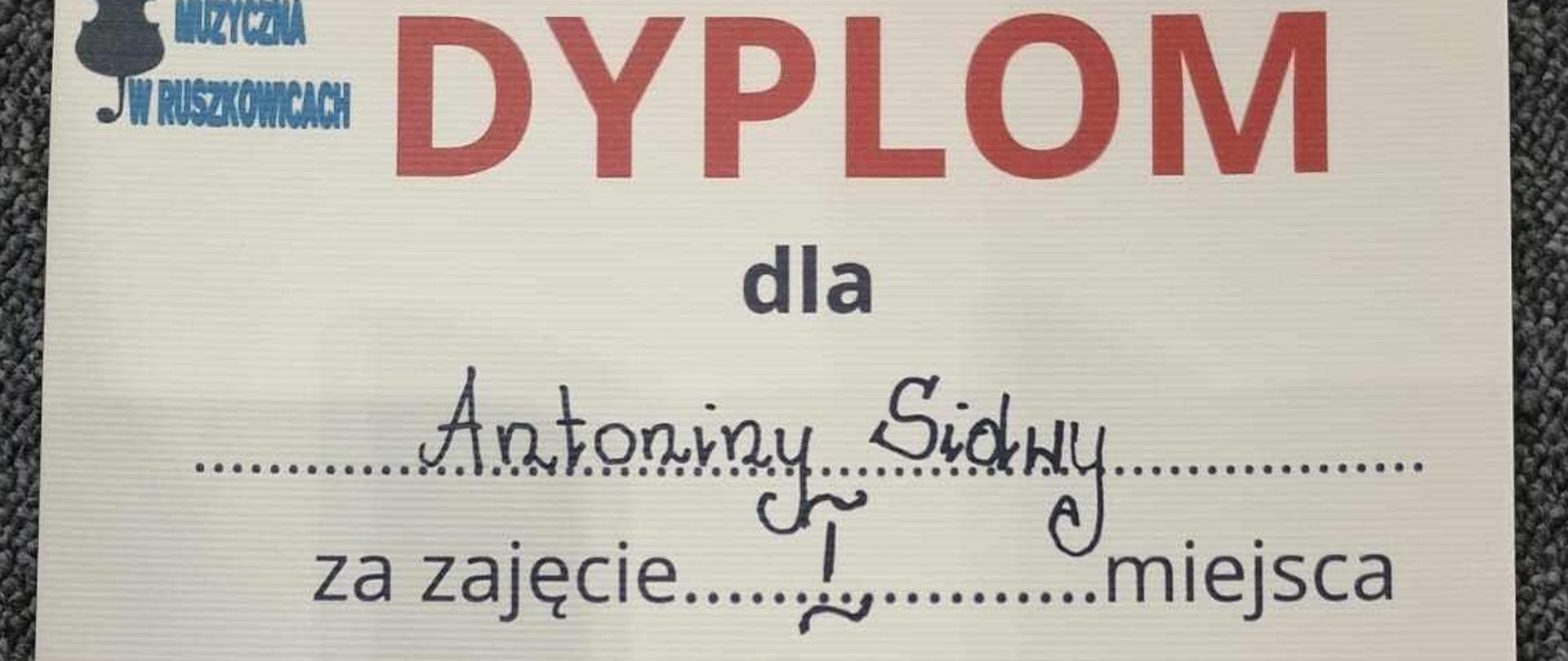 Zdjęcie przedstawia dyplom za zajęcie pierwszego miejsca w konkursie wiedzy o kompozytorach na środku dyplomu zdjęcie Witolda Lutosławskiego poniżej podpisy komisji.