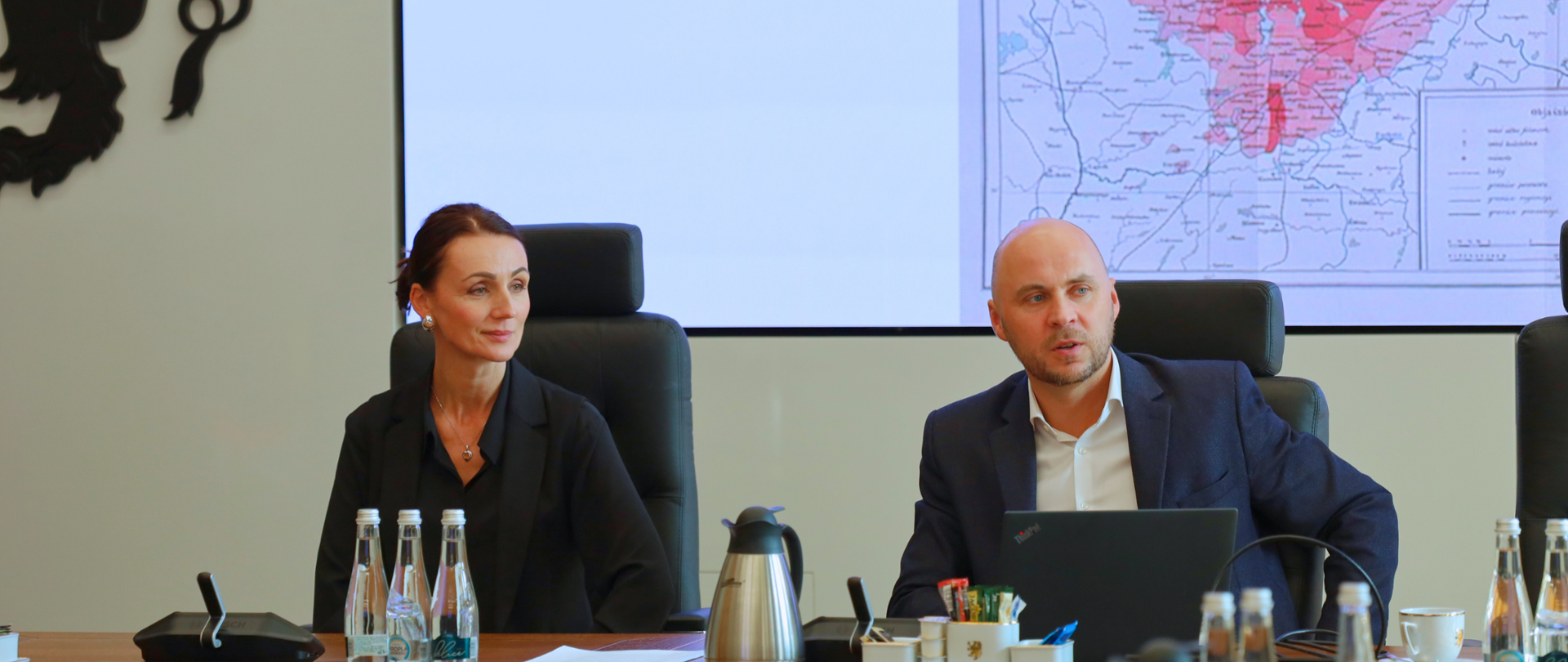 dwie osoby - kobieta i mężczyzna siedza przy biurku, w tle mapa woj. pom.