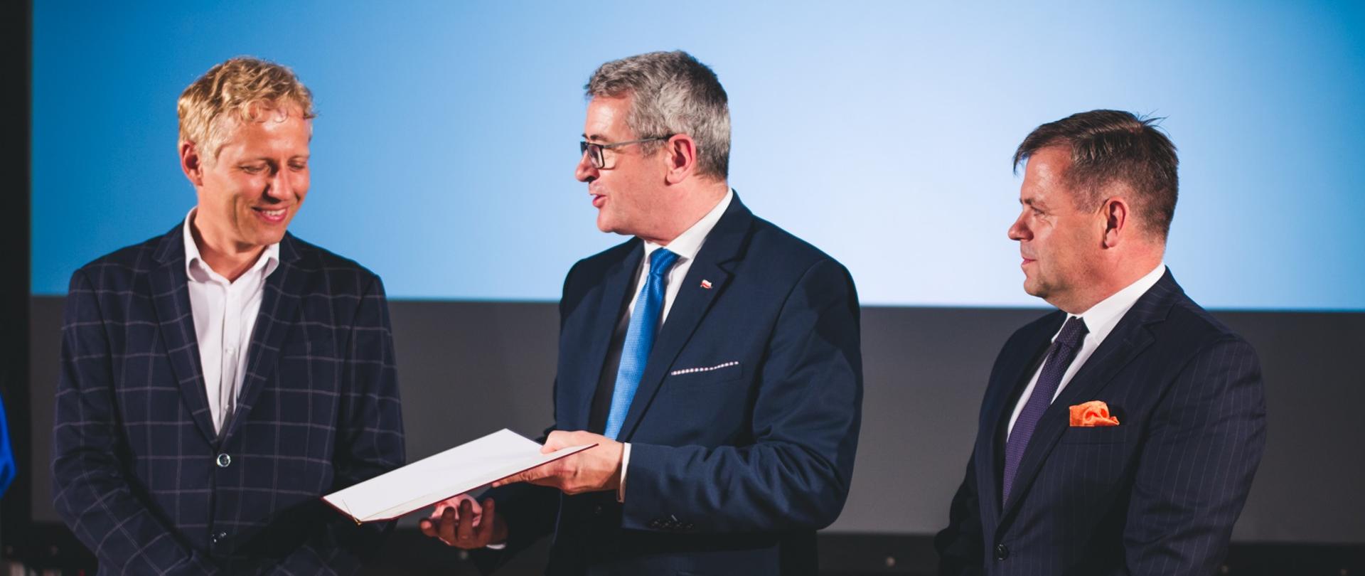 Na zdjęciu minister i przedstawiciele Łukasiewicz – PORT oglądają dokumenty.