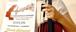 Zdjęcie przedstawia uczennicę ze skrzypcami, trzymającą dyplom laureata III Ogólnopolskiego Konkursu "Talenty Muzyczne 2025".