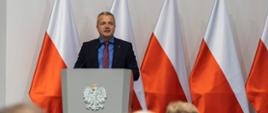 
Mężczyzna w garniturze stojący na tle biało-czerwonych flag