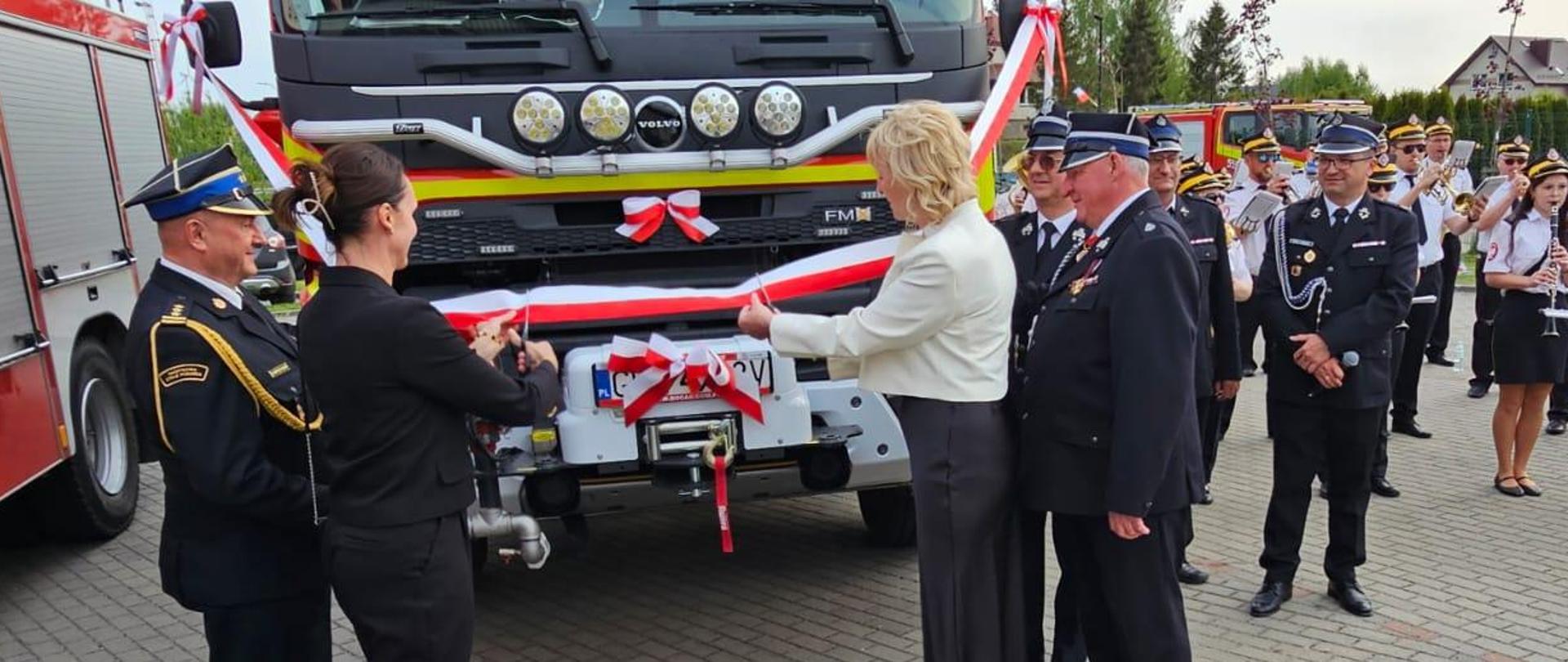 dwie osoby przecinają wstęgę podczas uroczystości przekazania nowych wozów strażackich