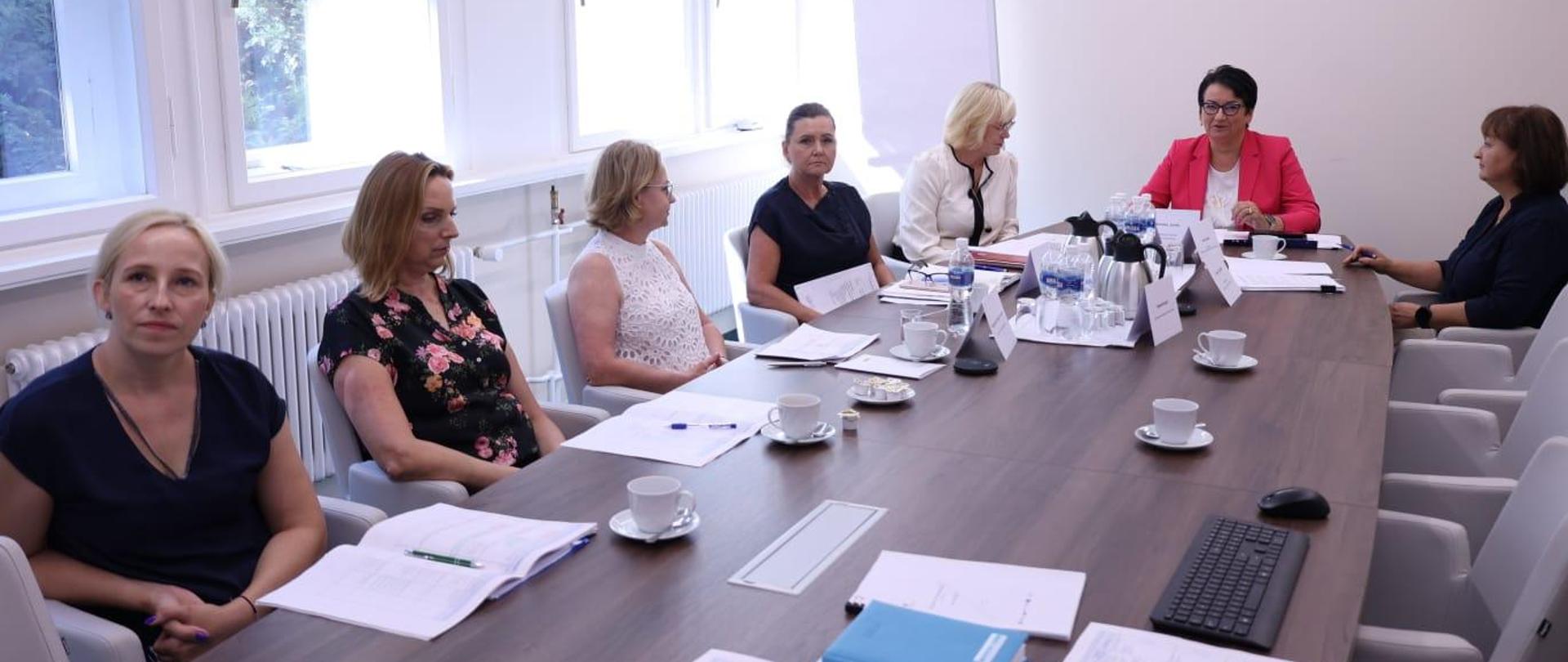 Uczestnicy (same kobiety) siedzą przy długim stole w sali konferencyjnej Opolskiego Urzędu Wojewódzkiego. 