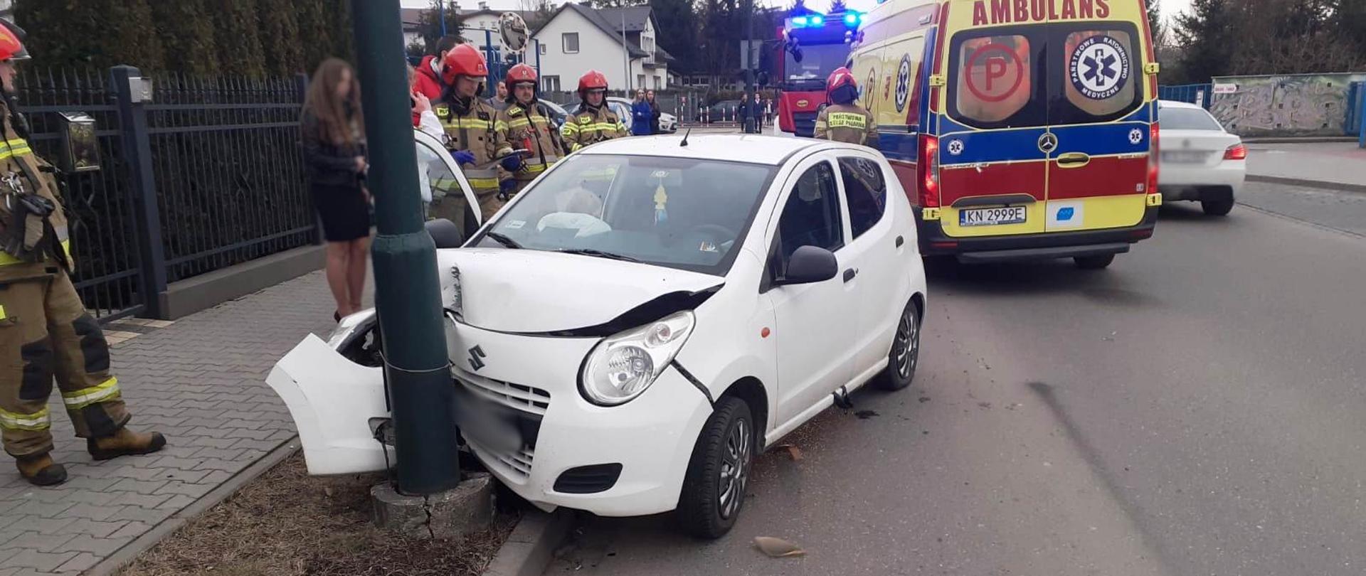 Samochód osobowy, który uderzył w latarnię. Obok strażacy oraz karetka Pogotowia Ratunkowego. 