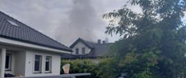 Budynek mieszkalny, nad budynkiem dym i para wodna. Zdjęcie w ciągu dnia. Przed budynkiem ogrodzenia.