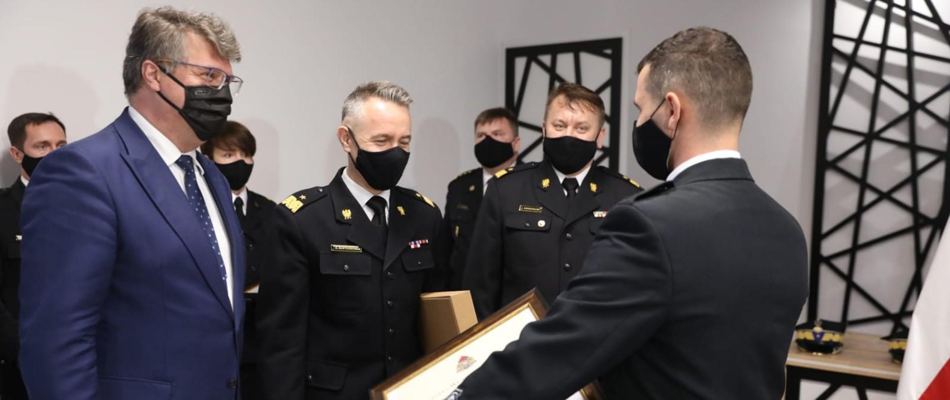 Pan minister Maciej Wąsik, wraz z komendantem głównym i komendantem wojewódzkim wręczają druhowi OSP akt włączenia do ksrg.