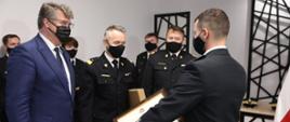 Pan minister Maciej Wąsik z komendantem głównym i komendantem wojewódzkim wręczają druhowi osp akt włączenia do ksrg.