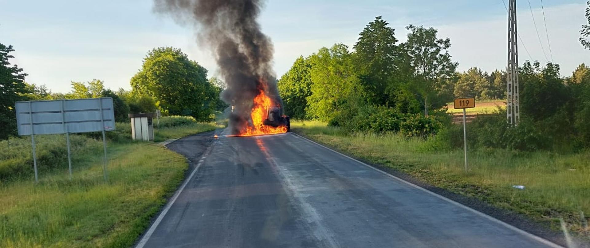 Zdjęcie przedstawia pożar harwestera na drodze.