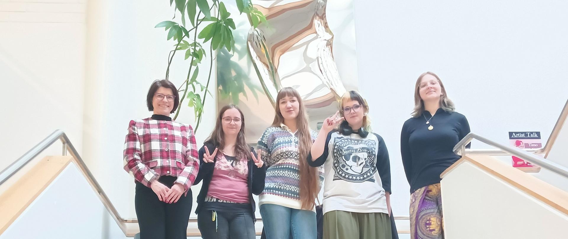 Zdjęcie przedstawia grupę sześciu osób ustawionych na szczycie klatki schodowej we wnętrzu publicznego budynku.