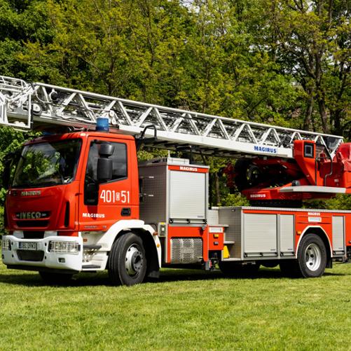 Samochód specjalny z drabiną mechaniczną marki IVECO Magirus oznaczony numerem „401[D]51”. Na podwoziu zamontowana jest długa, złożona drabina ratownicza z koszem na końcu, sygnowana logo „MAGIRUS”. Pojazd stoi na trawiastym tle.