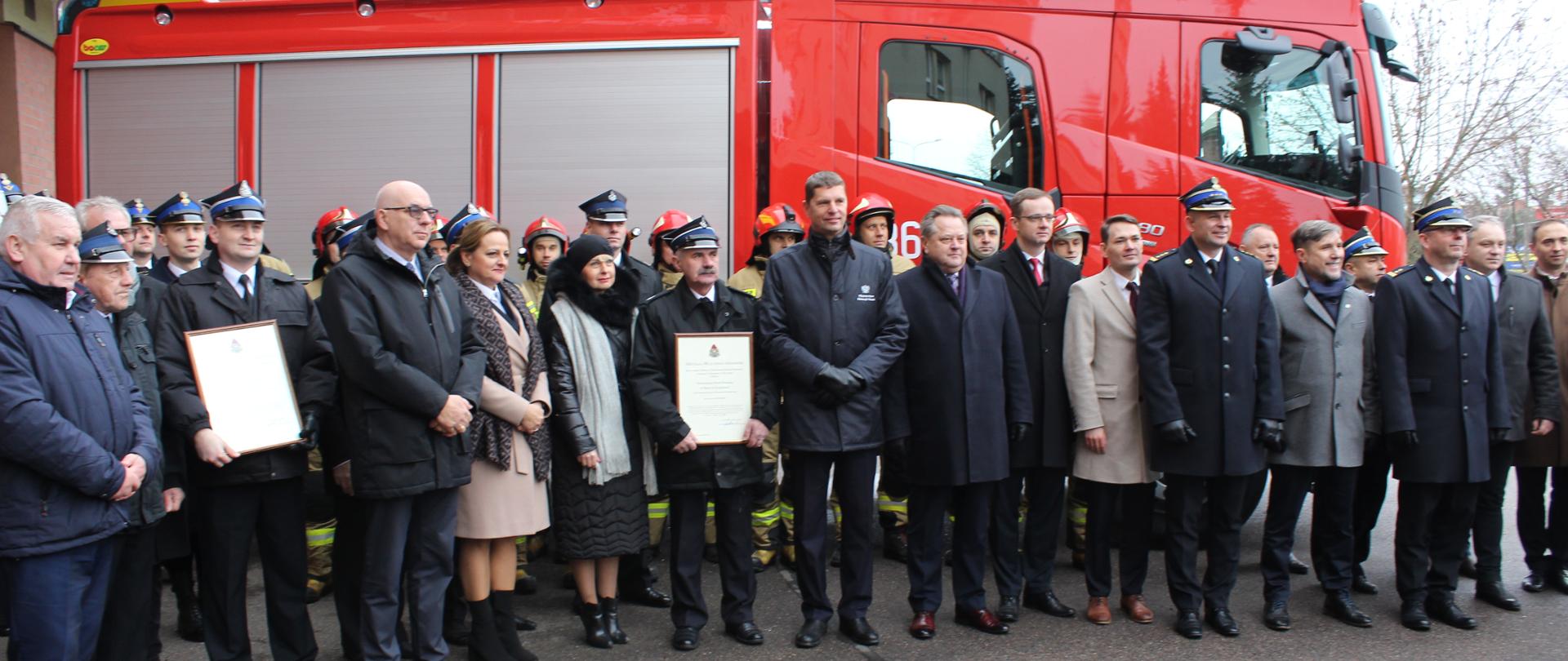 Wszyscy zaproszeni goście pozują do zdjęcia na tle nowego samochodu ratowniczo-gaśniczego