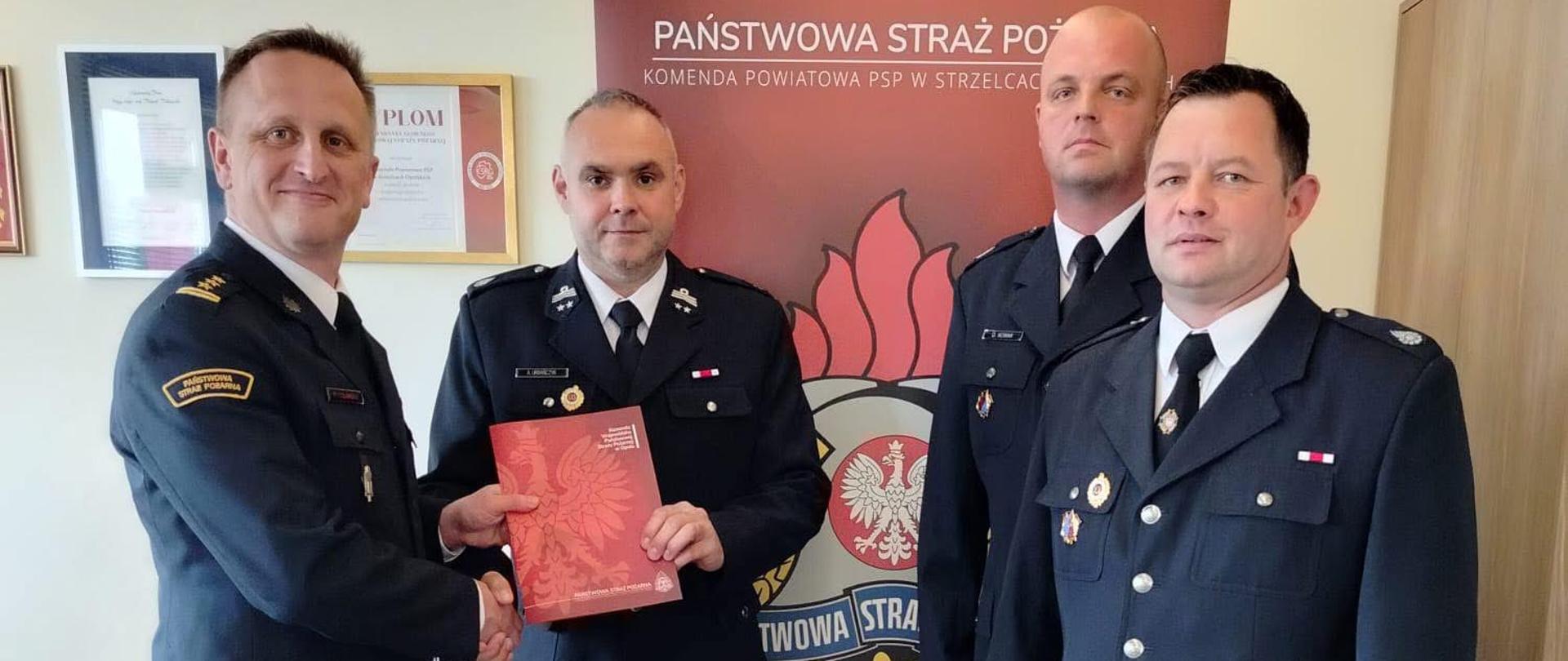 Na zdjęciu znajdują się strażacy w mundurach wyjściowych trzymający w ręku dyplom