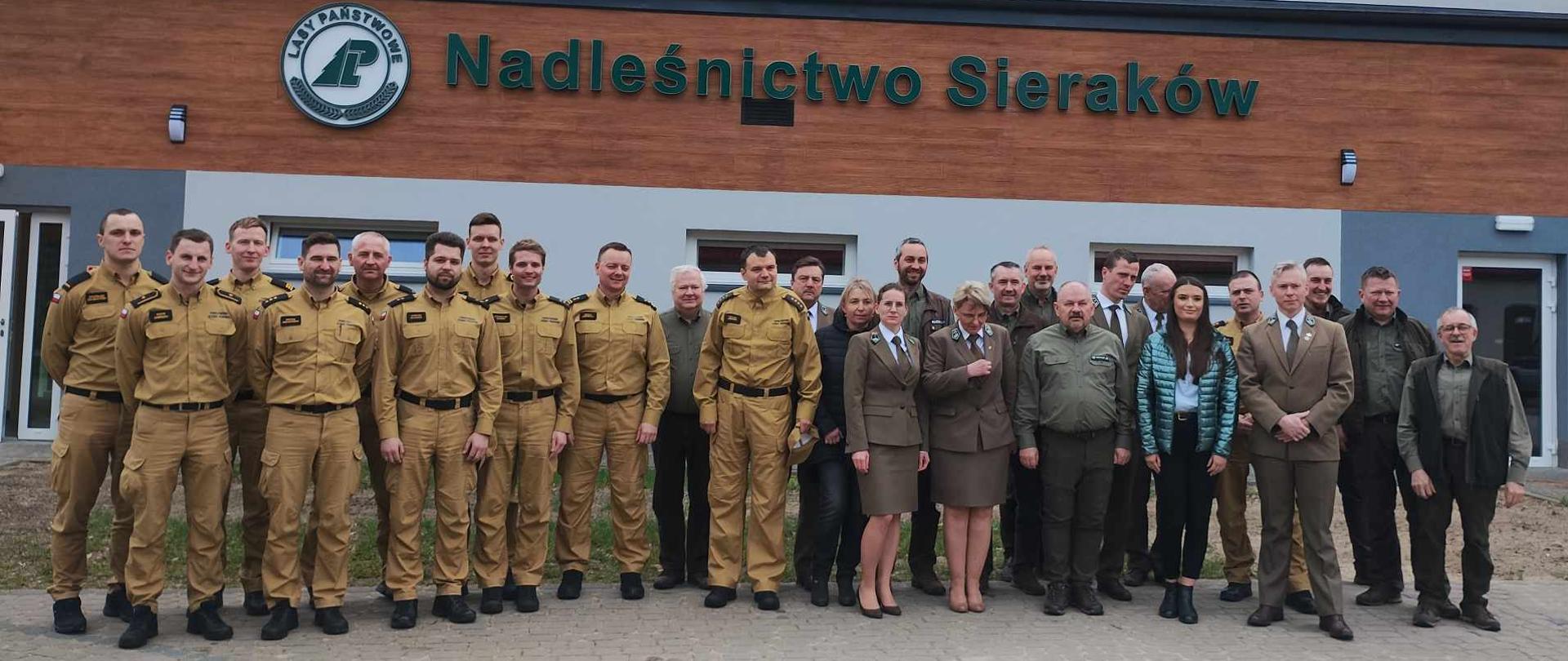 zdjęcie grupowe strażaków i leśników przed budynkiem nadleśnictwa
