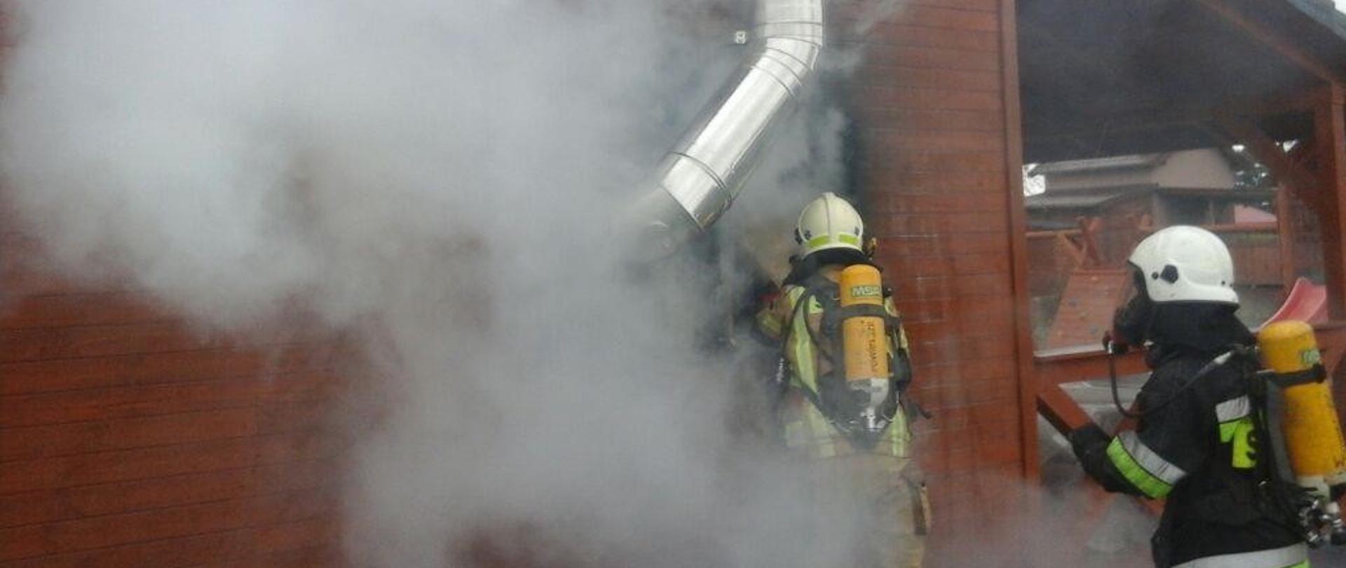 Drewniany budynek altany, zadymienie i dwoje strażaków podczas gaszenia pożaru.