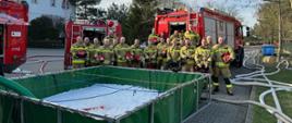 Zdjęcie pamiątkowe na zakończenie warsztatów. Widać zbiorniki i samochody pożarnicze oraz uczestników szkolenia