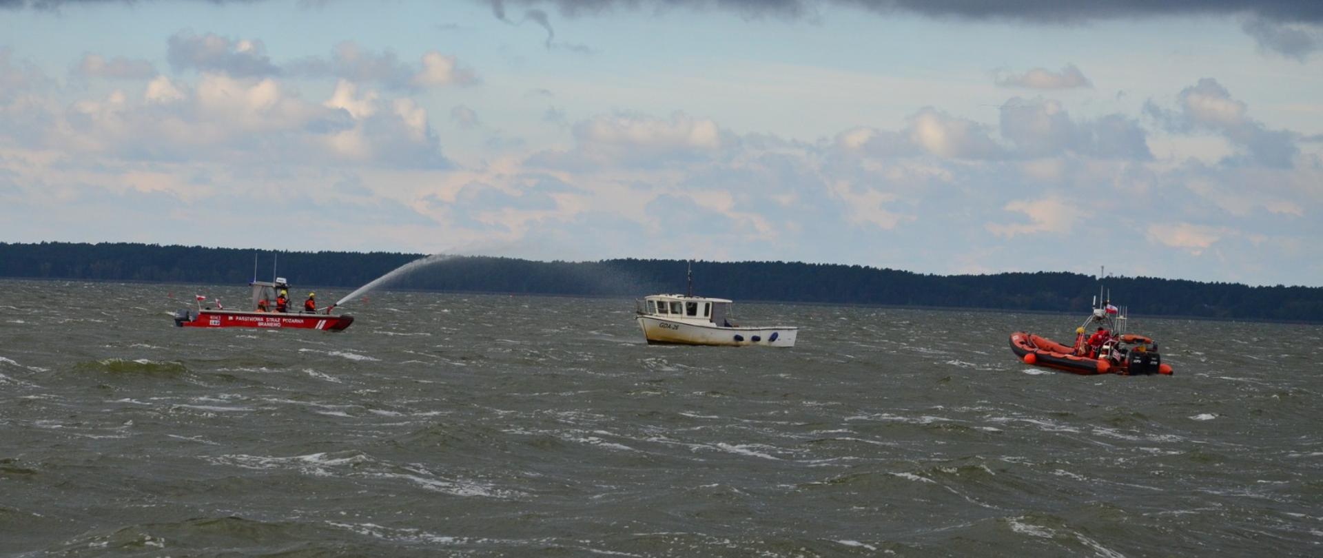 Na wodzie Zalewu Wiślanego stoją trzy łodzie. Z prawej i lewej czerwone a po środku biała. Pochmurno w oddali brzeg.