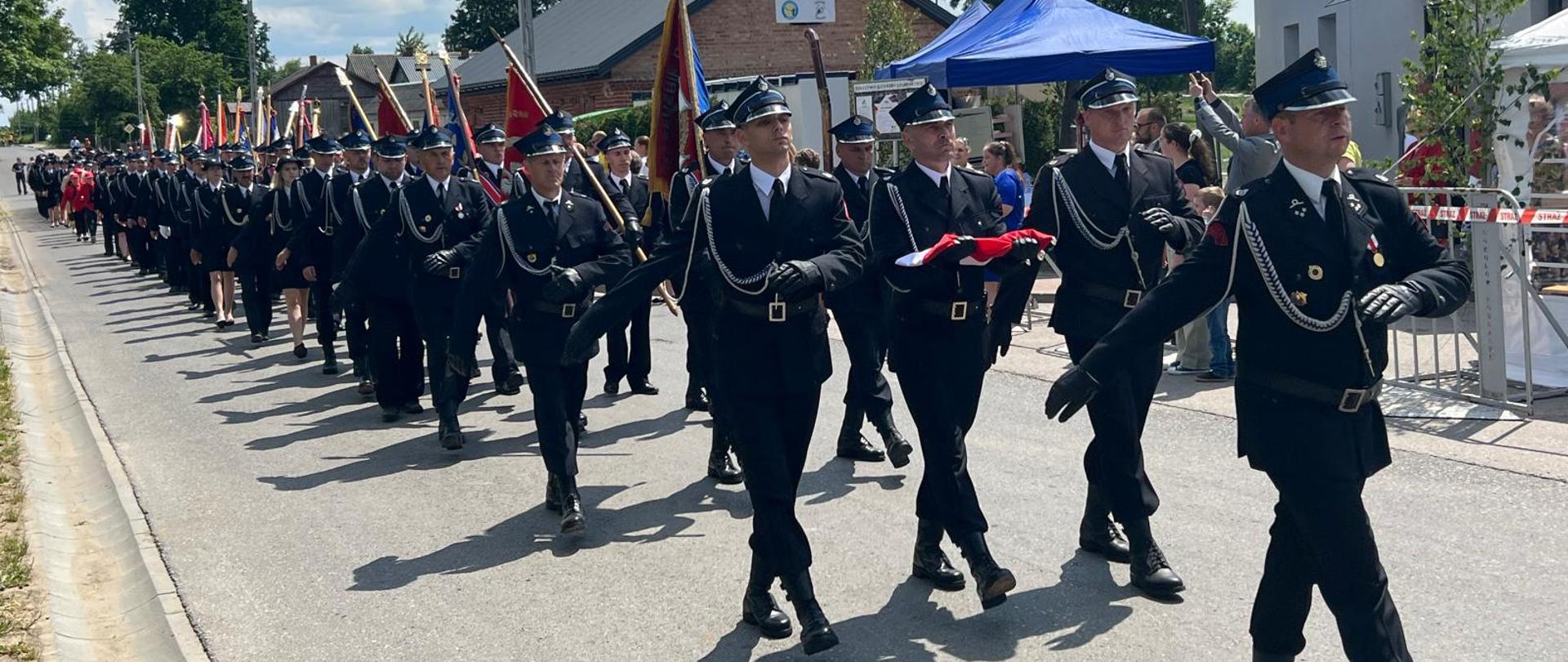Uroczysty apel z okazji 100-lecia jednostki Ochotniczej Straży Pożarnej w Dzierzbach (powiat sokołowski) - na zdjęciu przemarsz strażaków w mundurach wyjściowych na plac przed remizę OSP