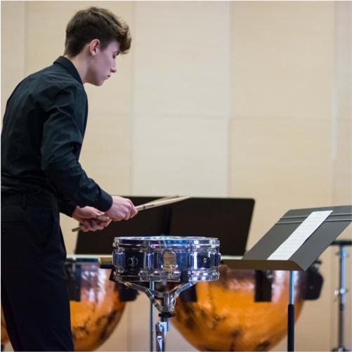 Grafika przedstawia osobę grającą na werblu na tle kotłów