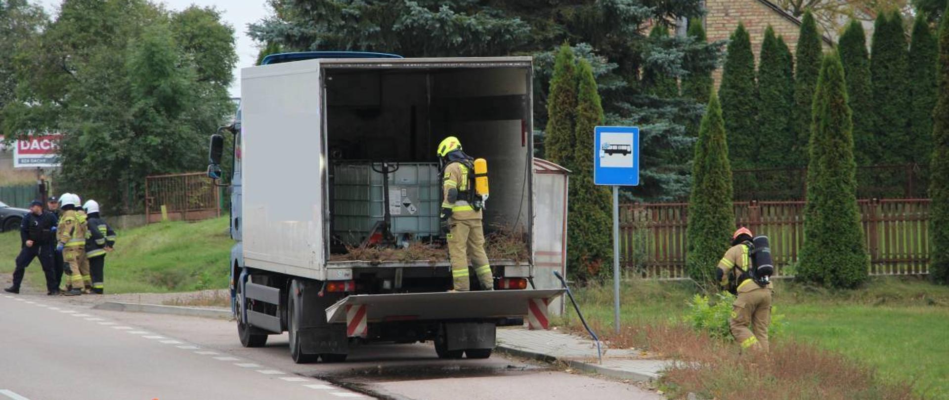 strażacy neutralizujący wyciek żrącej substancji z samochodu ciężarowego stojącego na poboczu DK 63