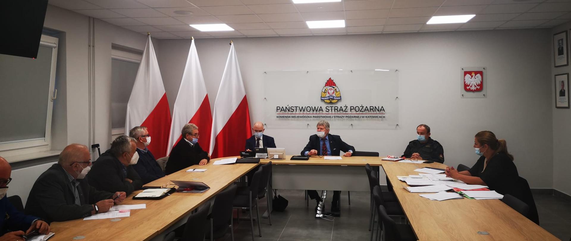 Przy stole prezydialnym prezes Zarządu Oddziału Wojewódzkiego ZOSP RP - gen. brygadier w st. spocz. Zbigniew Meres, wiceprezes Zarządu Oddziału Wojewódzkiego ZOSP RP, poseł na Sejm – Waldemar Andzel, wiceprezes Zarządu Oddziału Wojewódzkiego ZOSP RP, członek Zarządu Głównego - Rafał Glajcar, członek Zarzadu Głównego ZOSP RP - Henryk Kiepura, zastępca Śląskiego Komendanta Wojewódzkiego PSP - st. bryg. Bogdan Jędrocha. W tle napis Państwowa Straż Pożarna, Komenda Wojewódzka PSP, po lewej trzy biało-czerwone flagi. 