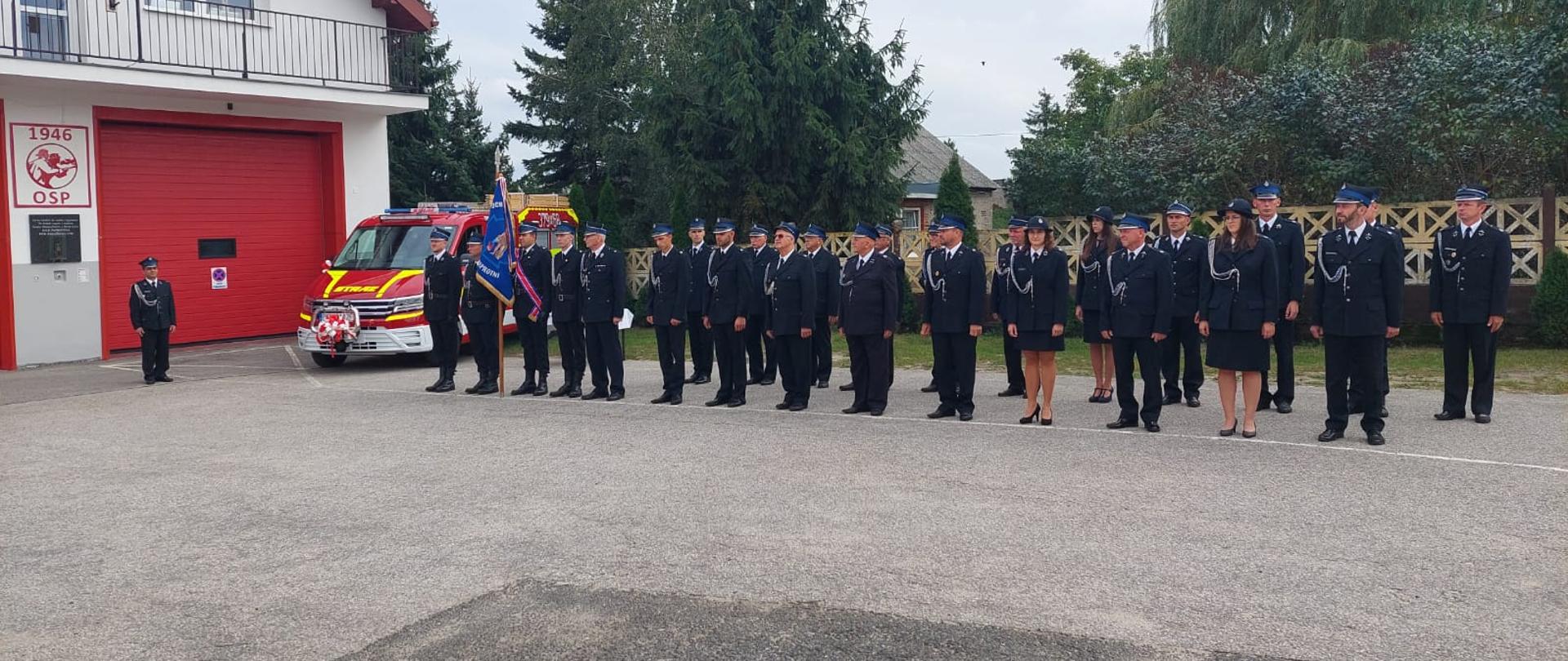 Strażacy OSP w mundurach galowych wraz z pocztem sztandarowym. W tle nowy samochód