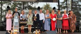 Grupa kilkunastu kobiet i mężczyzn – laureatów Konkursu oraz organizatorów Biesiady stoi na scenie. Pięć kobiet i jeden młody mężczyzna trzymają w rękach nagrody. Z tyłu znajduje się baner z napisem: „Biesiada Karpacka”.