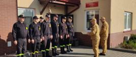 Strażacy stoją w szeregu przez budynkiem JRG 2. Naprzeciw komendant miejski PSP.