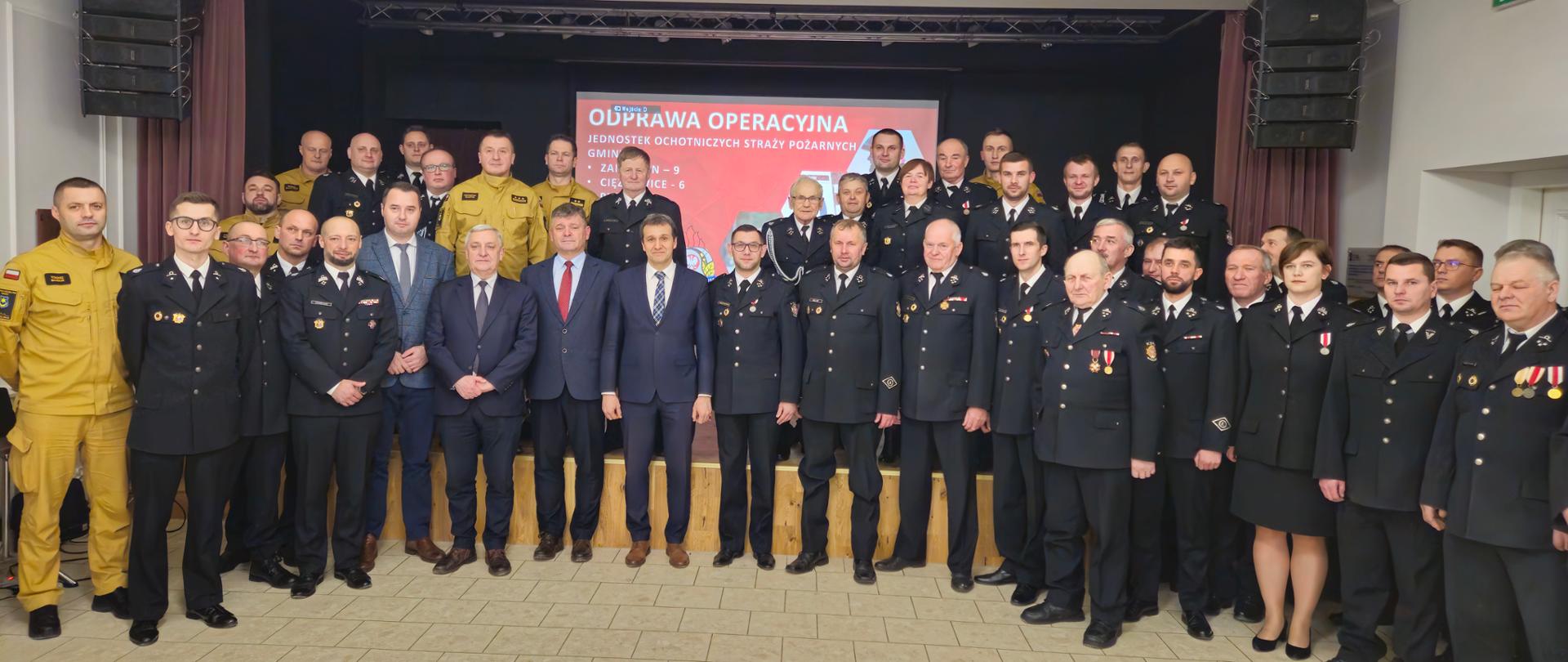 zdjęcie przedstawia grupę strażaków i samorządowców, w tle widoczna prezentacja