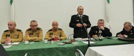 Jeden strażak przemawia podczas spotkania. Pozostali siedzą przy stole i przysłuchują się.