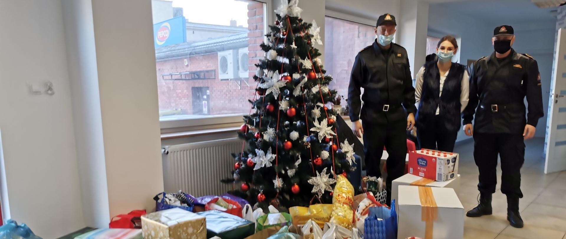 Strażacy stojący przy darach i przy choince. 
