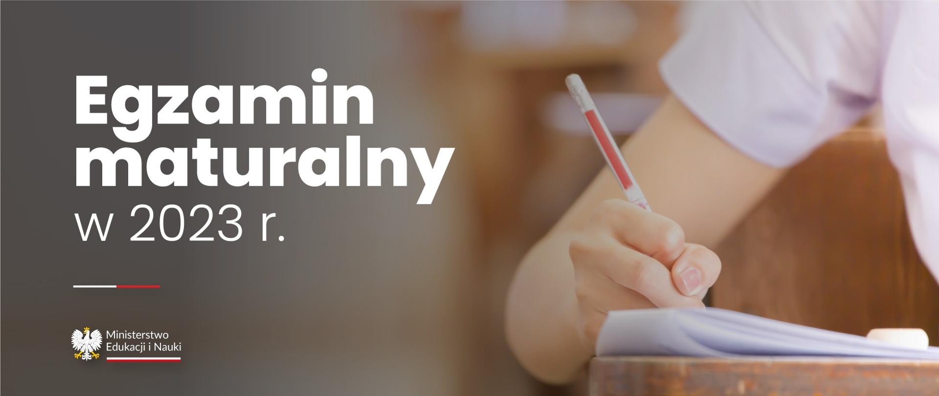Grafika - na szarożółtym tle ręka pisząca długopisem na kartce, obok napis Egzamin maturalny w 2023 r.
