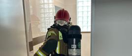 Zdjęcie przedstawia strażaka, który wchodzi do jednego z pomieszczeń, celem przeszukania pod kątem osób poszkdowanych.