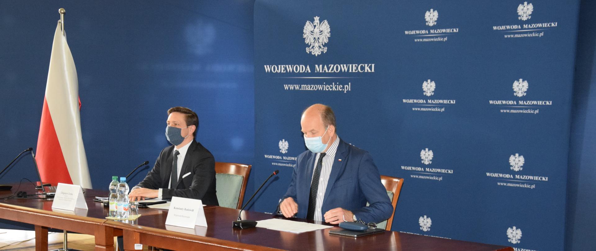 Na zdjęciu znajduje się dwóch mężczyzn siedzących za stołem. 