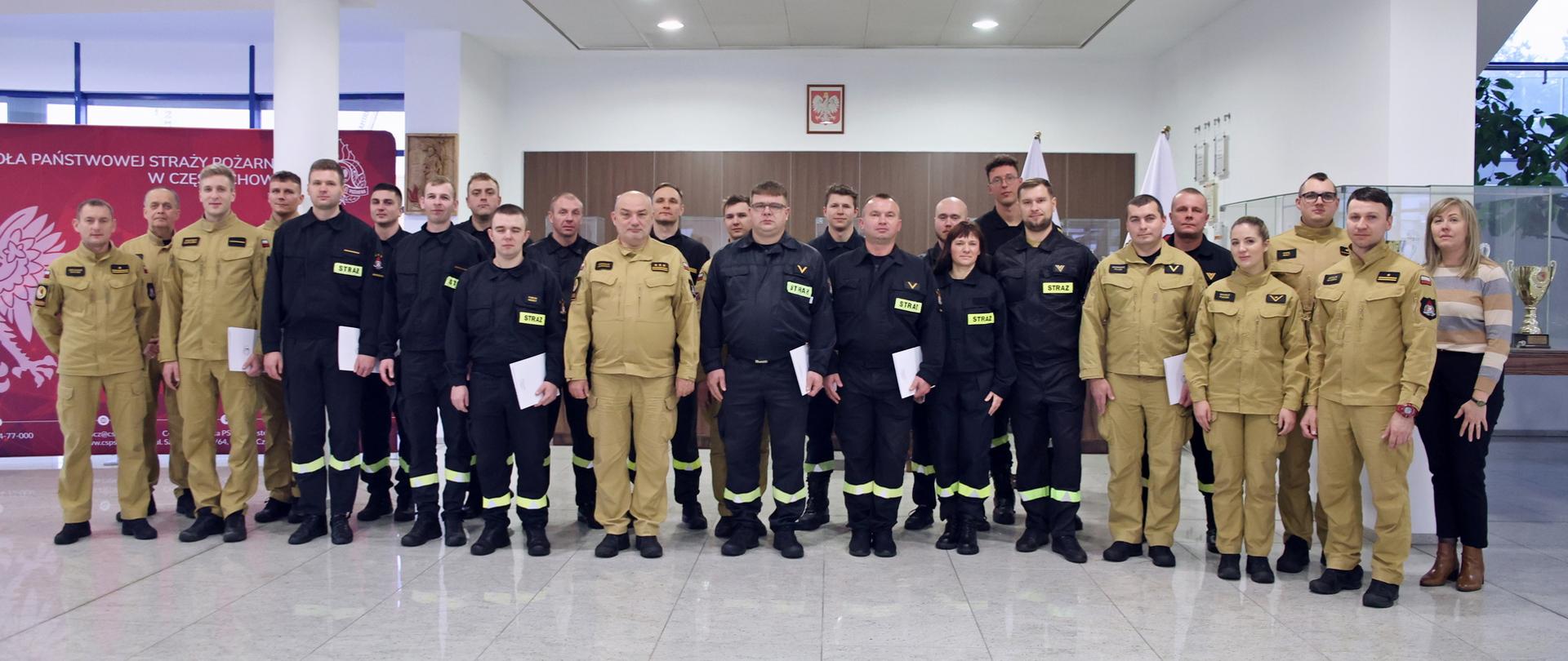 Pamiątkowe zdjęcie grupowe funkcjonariuszy PSP uczestniczących w szkoleniu w zakresie ratownictwa chemicznego i ekologicznego (19 osób) w towarzystwie Komendanta Centralnej Szkoły PSP, kobiety oraz funkcjonariuszki i czterech funkcjonariuszy CS PSP