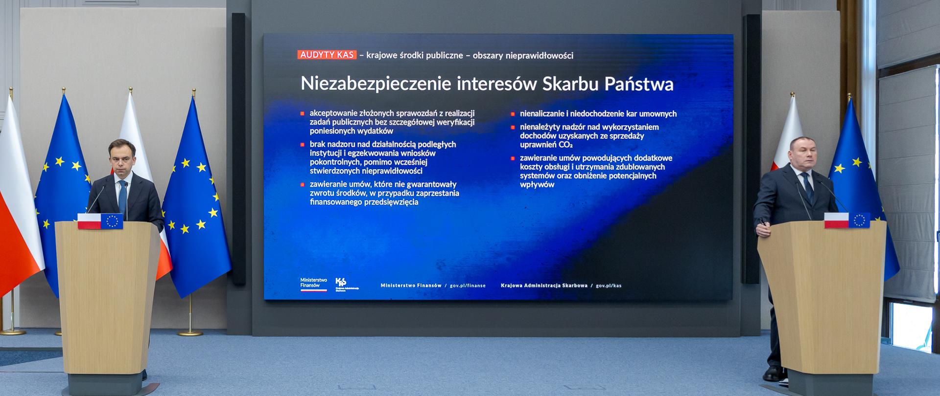 Na środku duży telebim z prezentacją. Po prawej przy mównicy Zastępca Szefa KAS. Po lewej Minister Finansów i Gospodarki. 