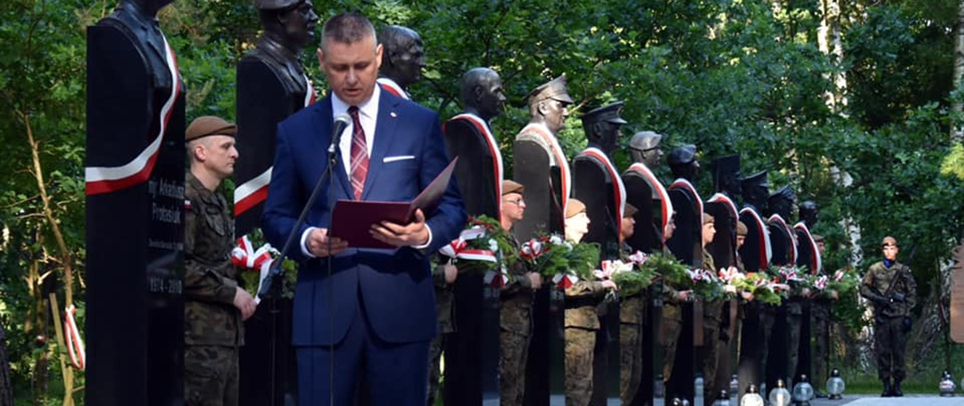 Na zdjęciu znajduje się mężczyzna czytający list, za nim stoją żołnierze