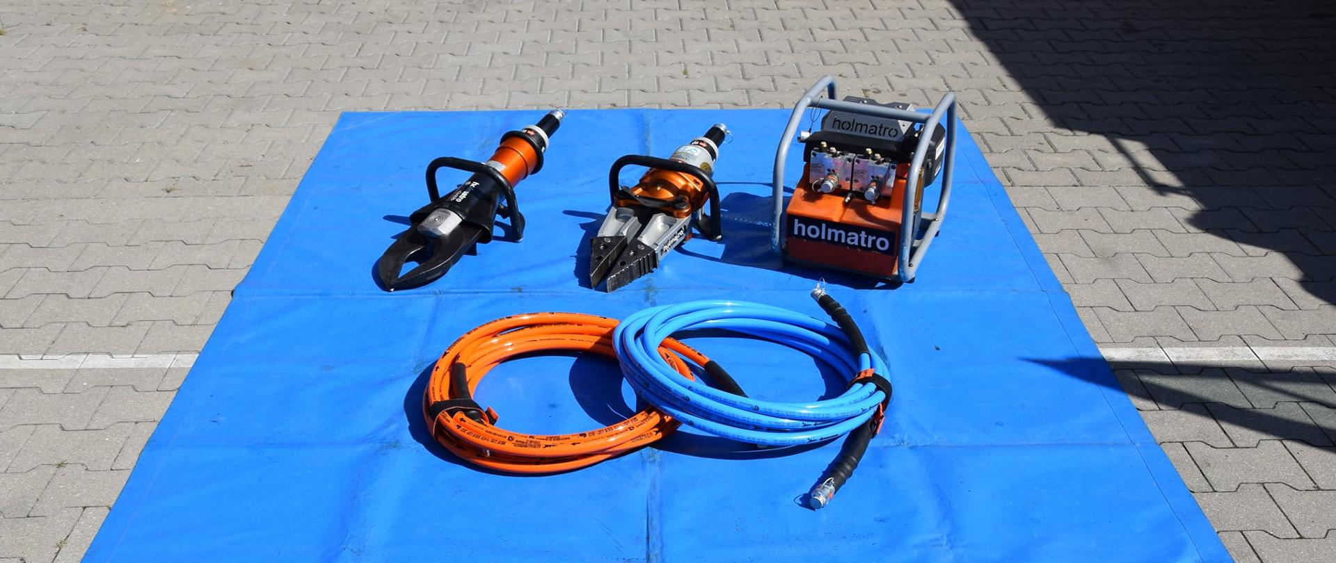 rozłożony zestaw hydrauliczny na placu przed komendą: pompa, nożyce, rozpieracz ramieniowy i 2 komplety węży