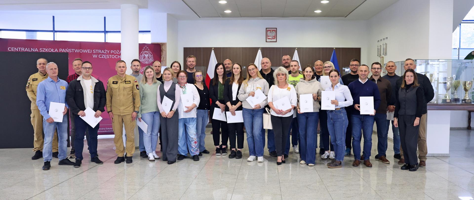 Pamiątkowe zdjęcie grupowe uczestników szkolenia aktualizującego inspektorów ochrony przeciwpożarowej (28 osób) w towarzystwie Zastępcy Komendanta CS PSP, kobiety oraz funkcjonariusza CS PSP