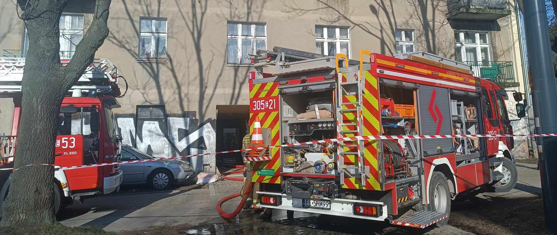 Samochód pożarniczy z rozwiniętą linią gaśniczą przed budynkiem wielorodzinnym