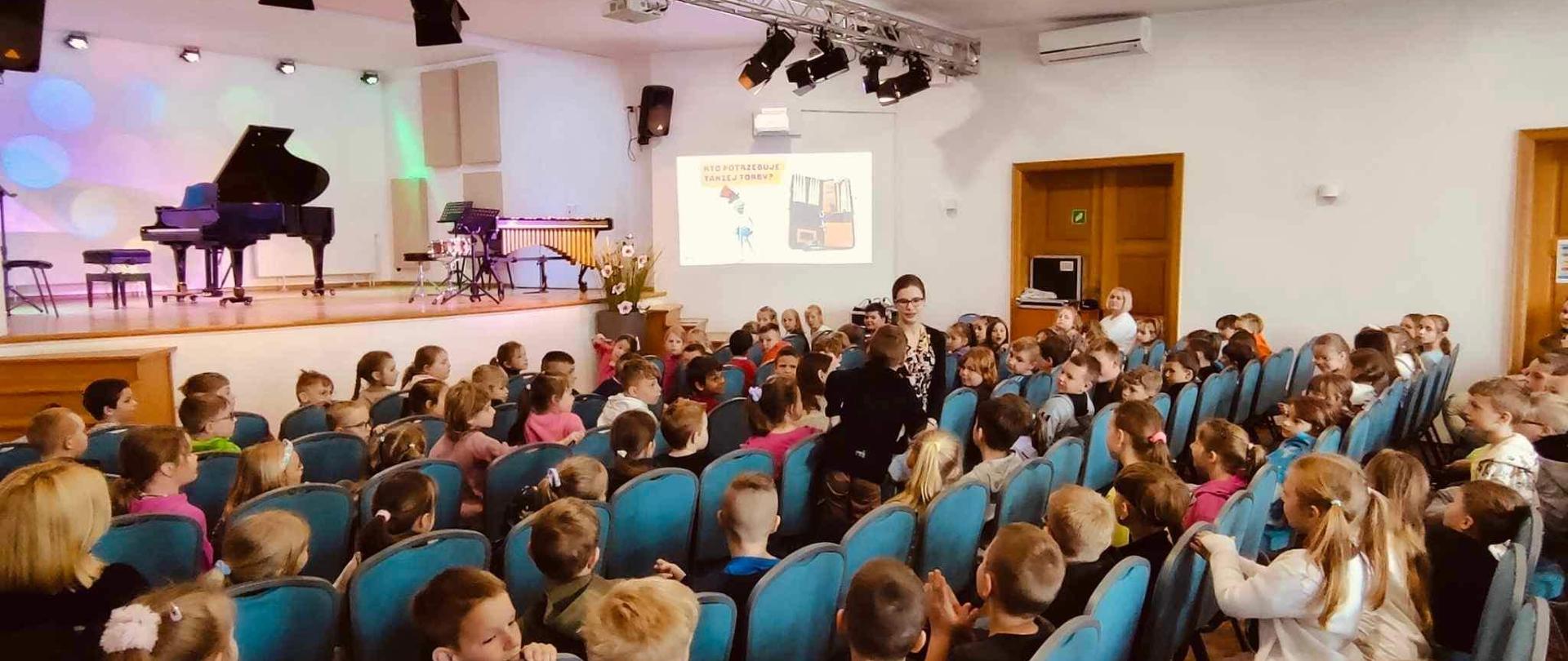Widok sali koncertowej wypełnionej po brzegi młodymi słuchaczami podczas koncertu edukacyjnego.