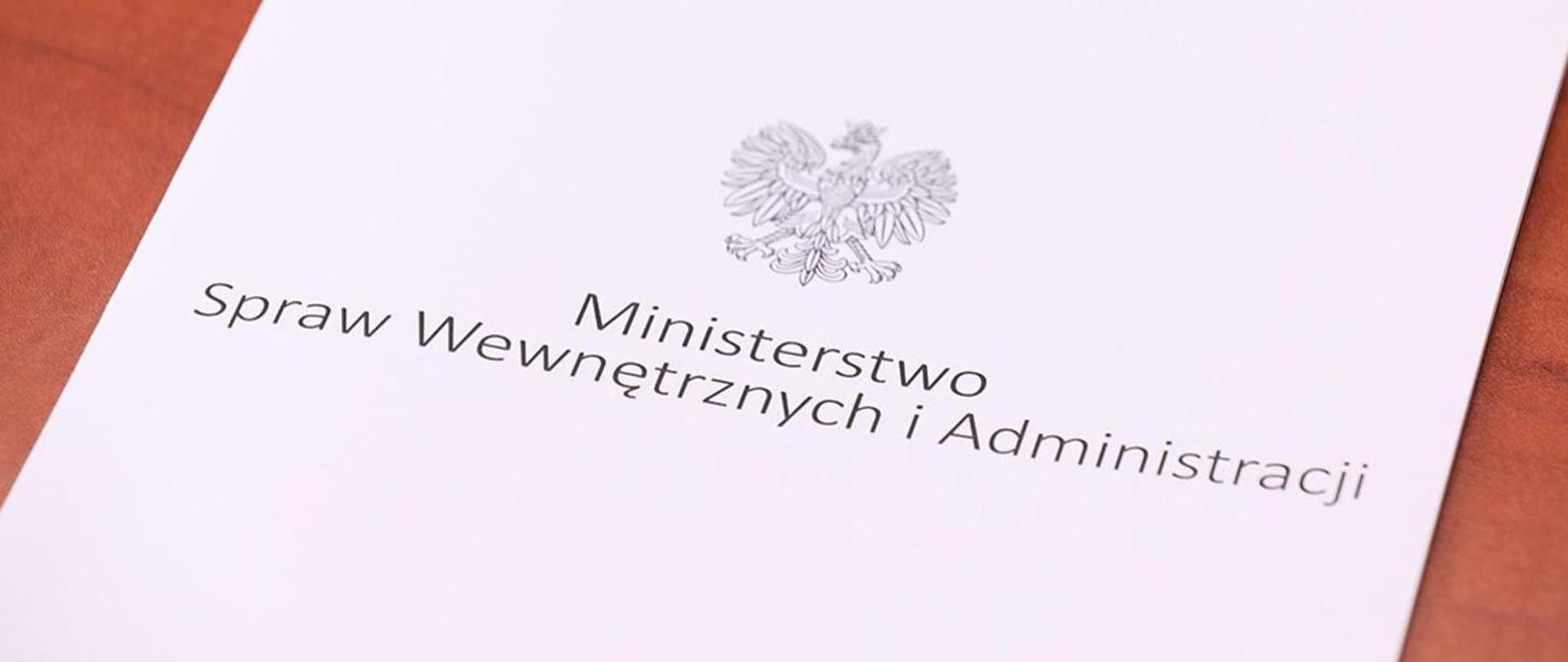 Widok teczki na stole. Na środku napis Ministerstwo Spraw Wewnętrznych i Administracji. Powyżej czarno-biały wizerunek orła (godło państwowe).