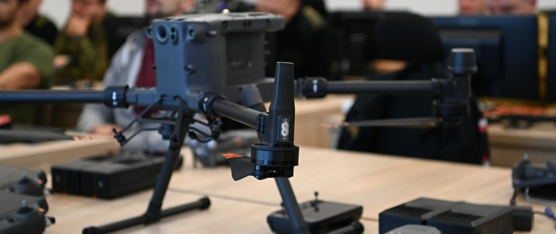 W sali dydaktycznej na ławce na pierwszym planie stoi dron - bezzałogowy statek powietrzny a tle słuchacze szkolenia siedzą podczas zajeć