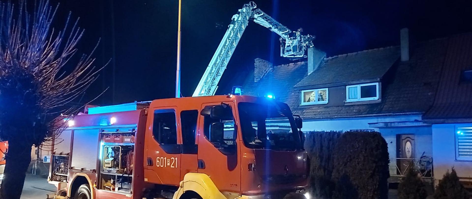 Na zdjęciu samochód ratowniczo gaśniczy, w oddali podnośnik pracujący przy kominie z ratownikami w koszu