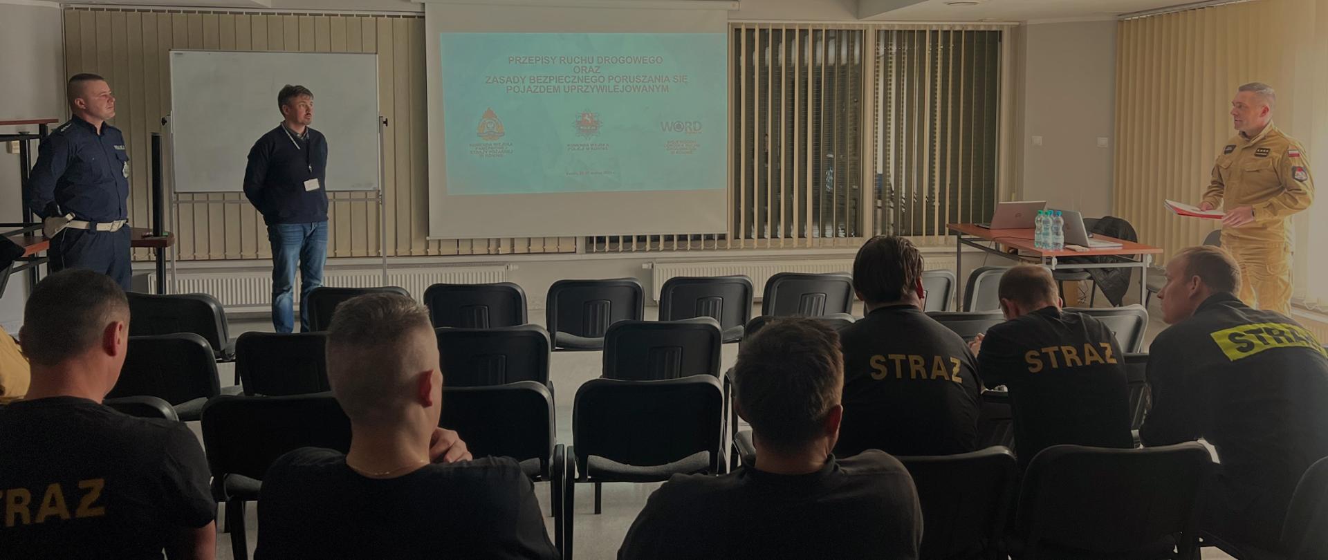 Zdjęcie przedstawia grupę strażaków, policjanta oraz pracownika z wojewódzkiego ośrodka ruchu drogowego w sali wykładowej podczas pogadanki.